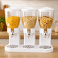 Dispensador de cereal triple en blanco, con tres depósitos llenos de distintos cereales, sobre una mesa de cocina