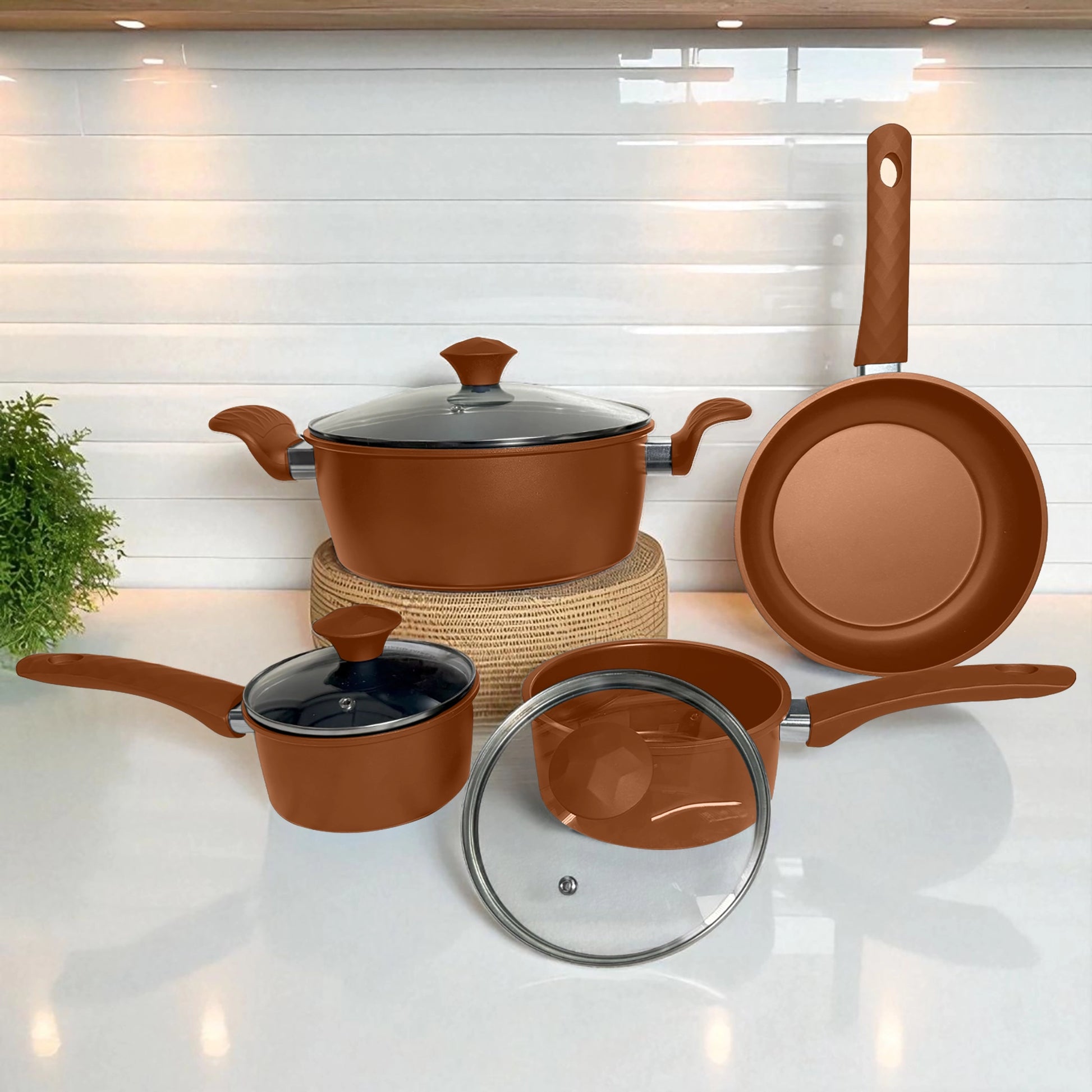 Set de ollas antiadherentes color bronce con tapas de vidrio, vista frontal completa sobre encimera de cocina moderna.