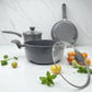 Set de cocina Big Home 5 piezas con cacerola, olla y sartén en fondo de mármol, rodeado de vegetales frescos.