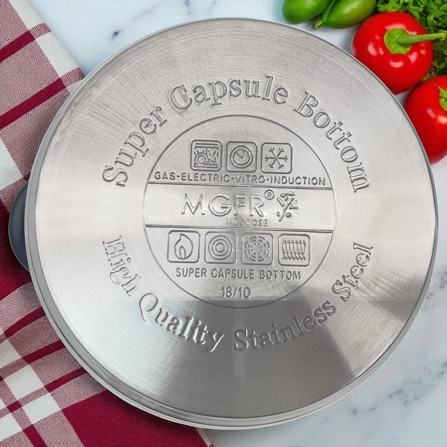 Sello inferior de olla MGFR con grabado super capsule bottom y compatibilidad universal de calor, sobre superficie marmoleada con verduras alrededor
