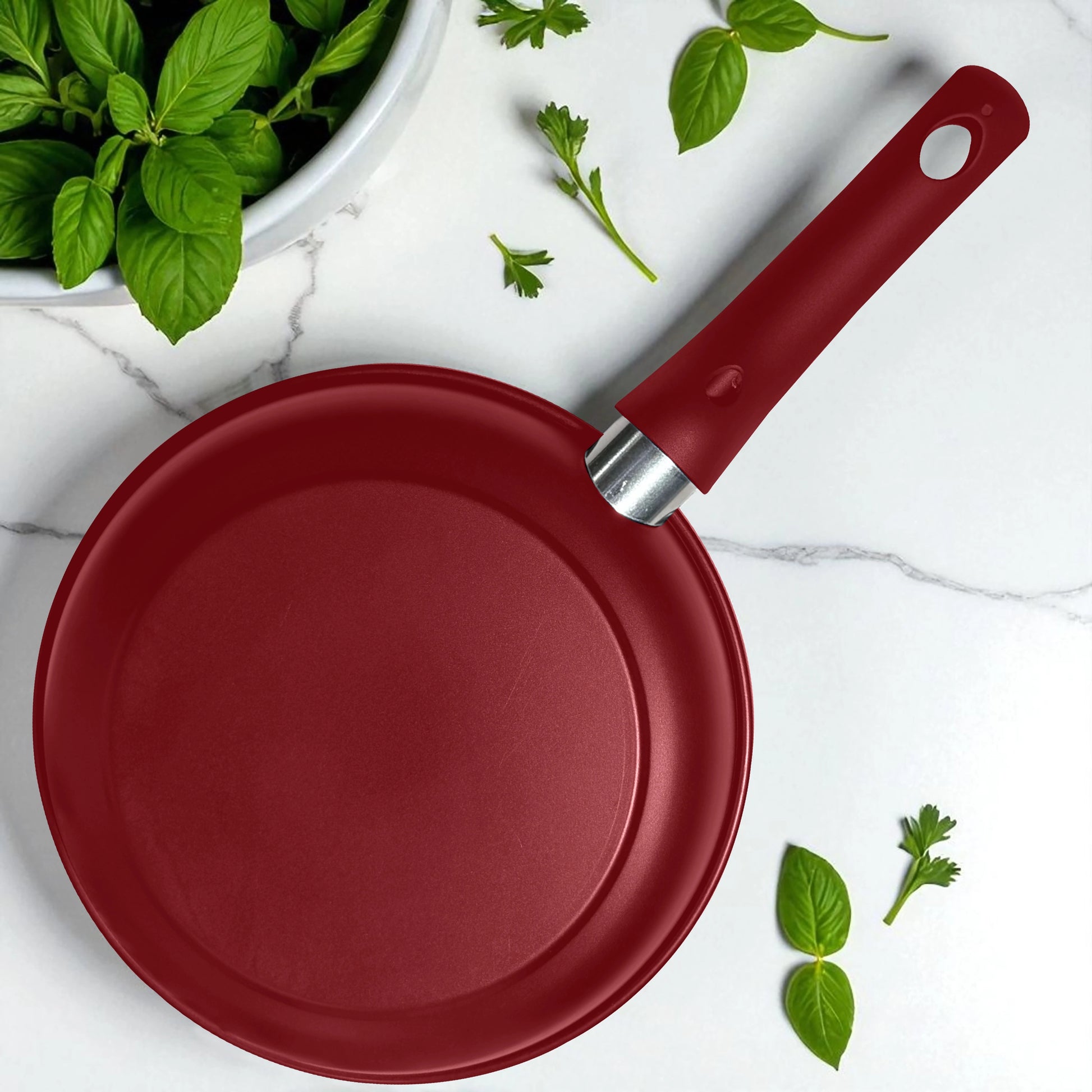 Vista superior del sartén de 14 cm BIG Home con acabado en rojo mate y mango ergonómico, sobre encimera con hojas verdes.