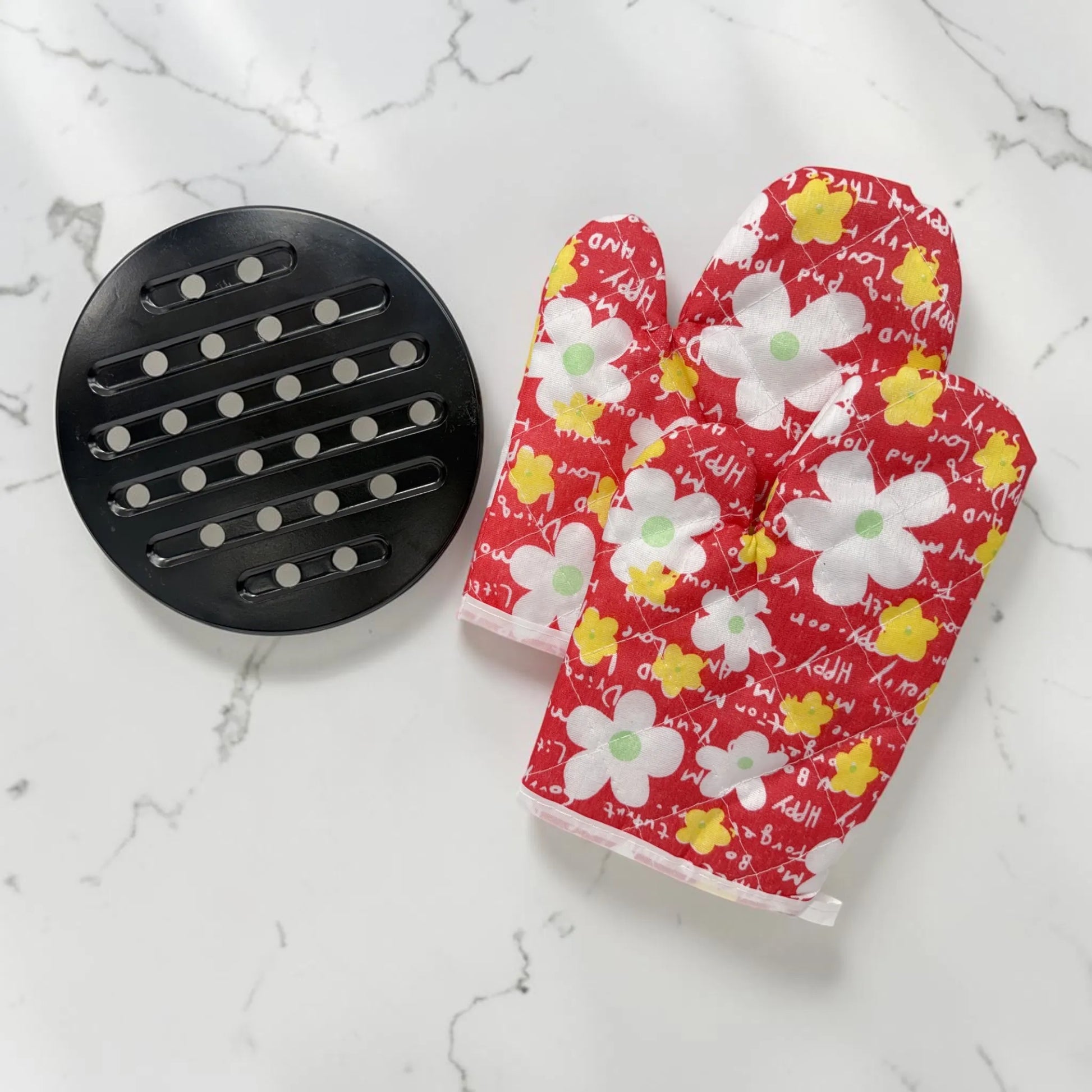 Accesorios incluidos del set de ollas Romania: base metálica negra redonda y dos guantes térmicos rojos con estampado floral.