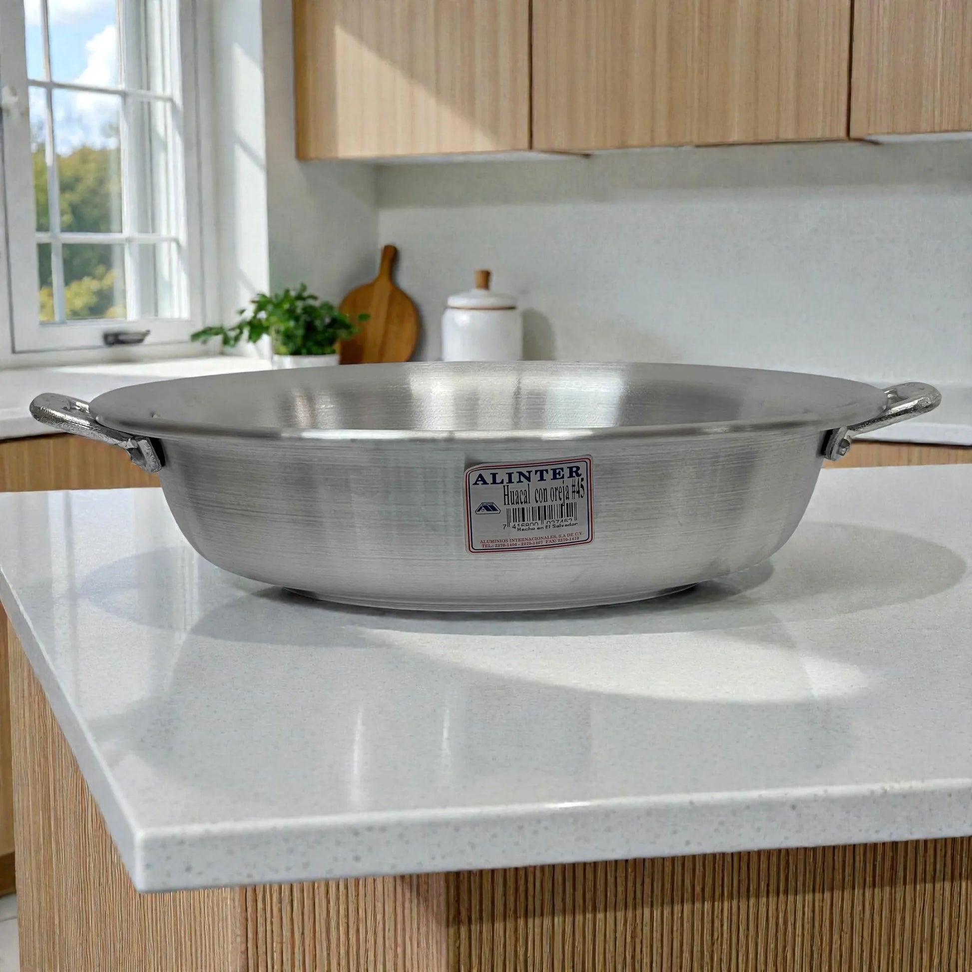 Huacal con oreja #45 marca Alinter en aluminio plateado, tipo sarten amplio y bajo con dos asas laterales, vista lateral sobre encimera de cocina.