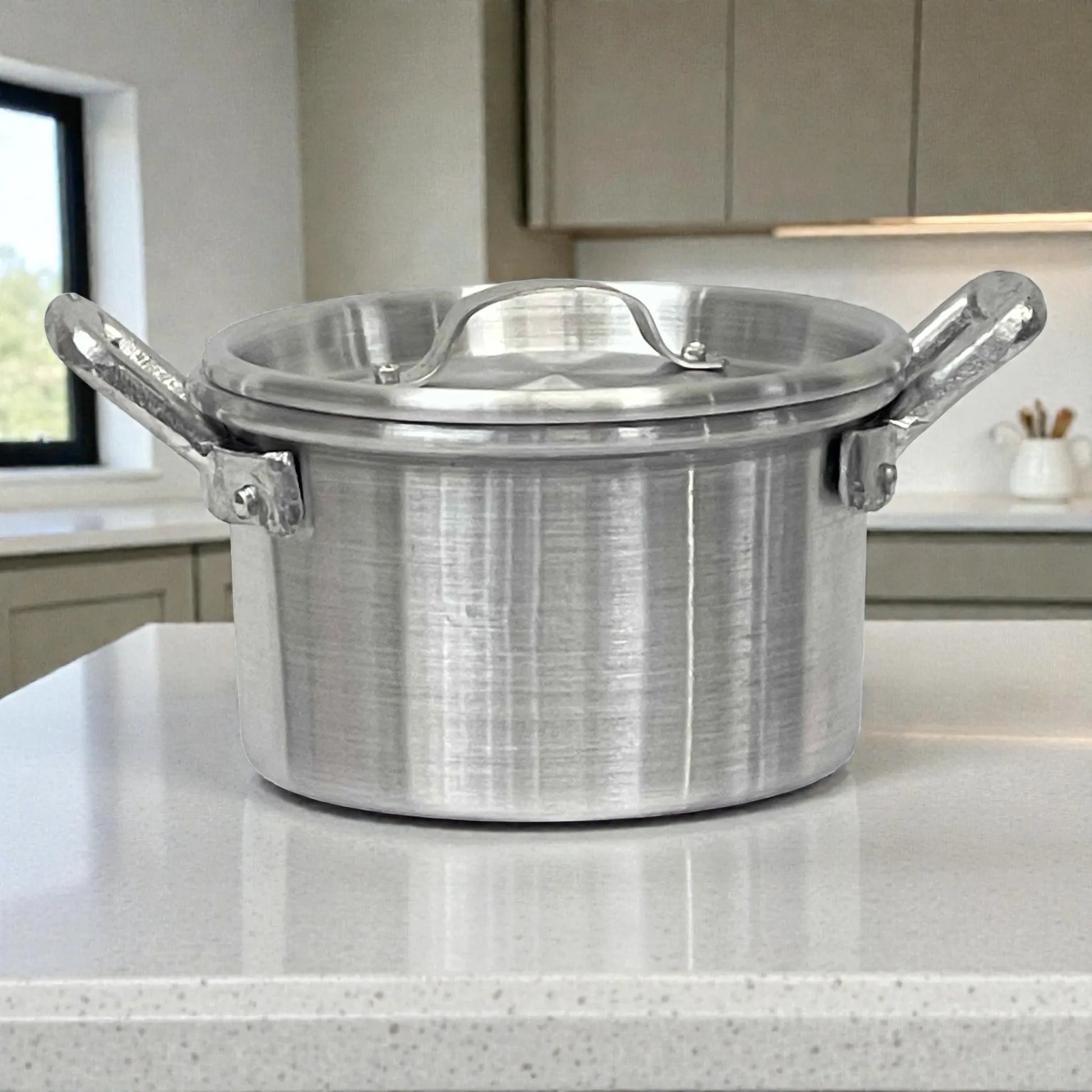 Olla de aluminio ALINTER con oreja #18 y tapa, color plateado, hecha en El Salvador, vista lateral/frontal sobre encimera de cocina.