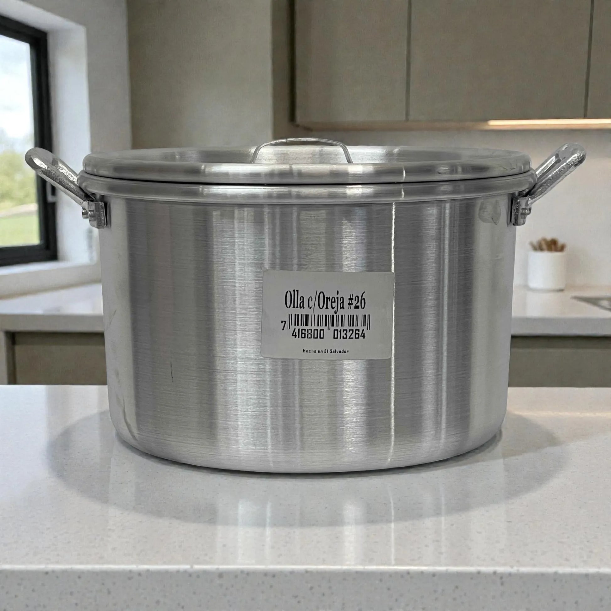 Olla de aluminio ALINTER con oreja #26 y tapa, color plateado, hecha en El Salvador, vista frontal sobre encimera de cocina.