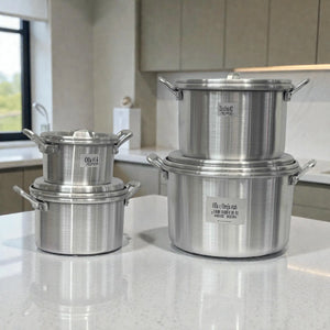 Set de 4 ollas de aluminio ALINTER con oreja y tapa (#14 #18 #22 #26), color plateado, hechas en El Salvador, apiladas sobre encimera en cocina.