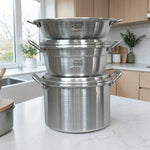 Set de cocina Alinter de aluminio (SKU OAO3824) apilado en encimera: huacal con oreja #45 arriba, arrocera #38 al centro y olla con oreja #38 abajo, color aluminio plateado con asas laterales.