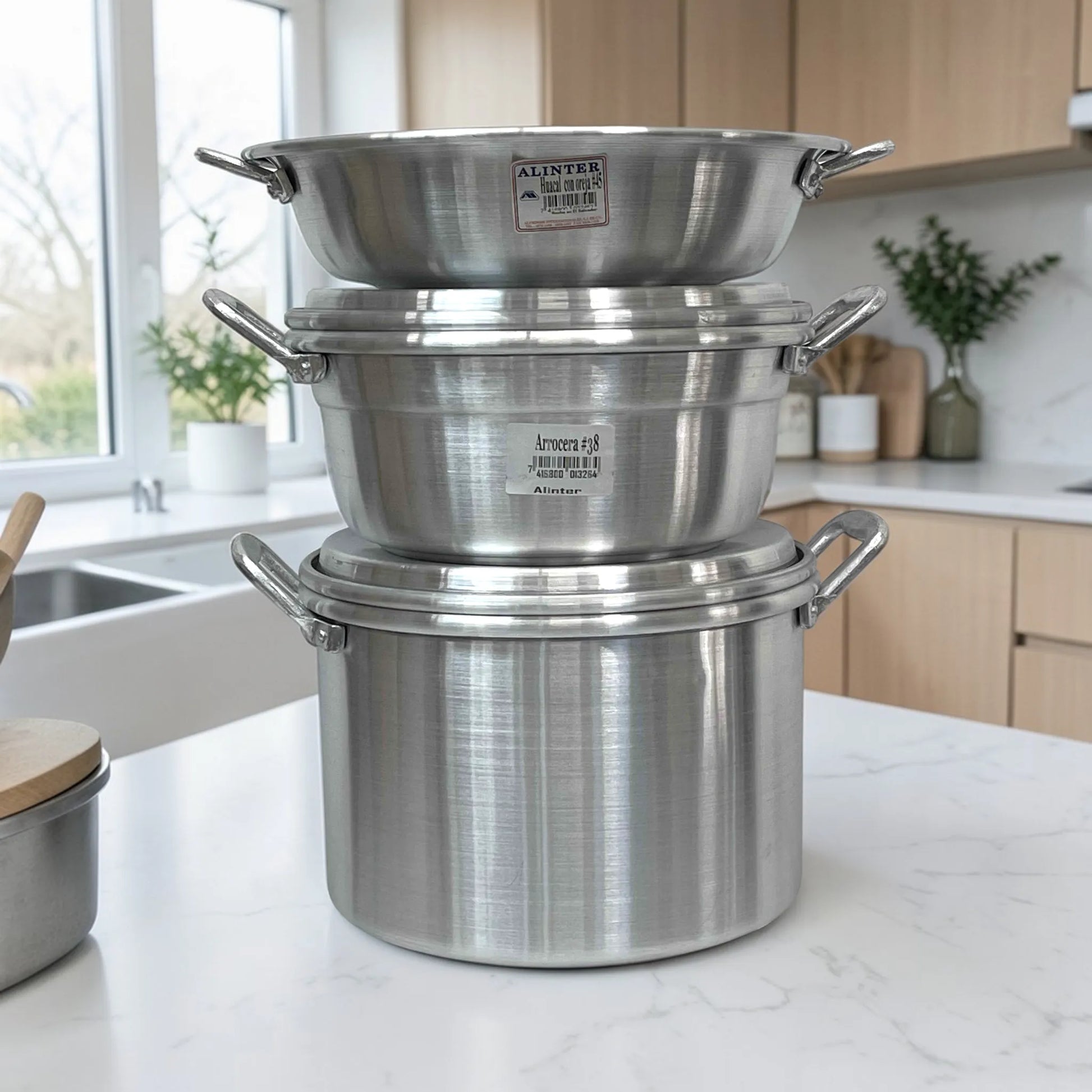 Set de cocina Alinter de aluminio (SKU OAO3824) apilado en encimera: huacal con oreja #45 arriba, arrocera #38 al centro y olla con oreja #38 abajo, color aluminio plateado con asas laterales.