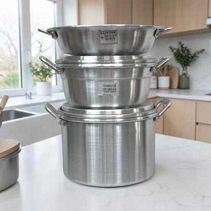 Set de cocina Alinter de aluminio (SKU OAO3824) apilado en encimera: huacal con oreja #45 arriba, arrocera #38 al centro y olla con oreja #38 abajo, color aluminio plateado con asas laterales.