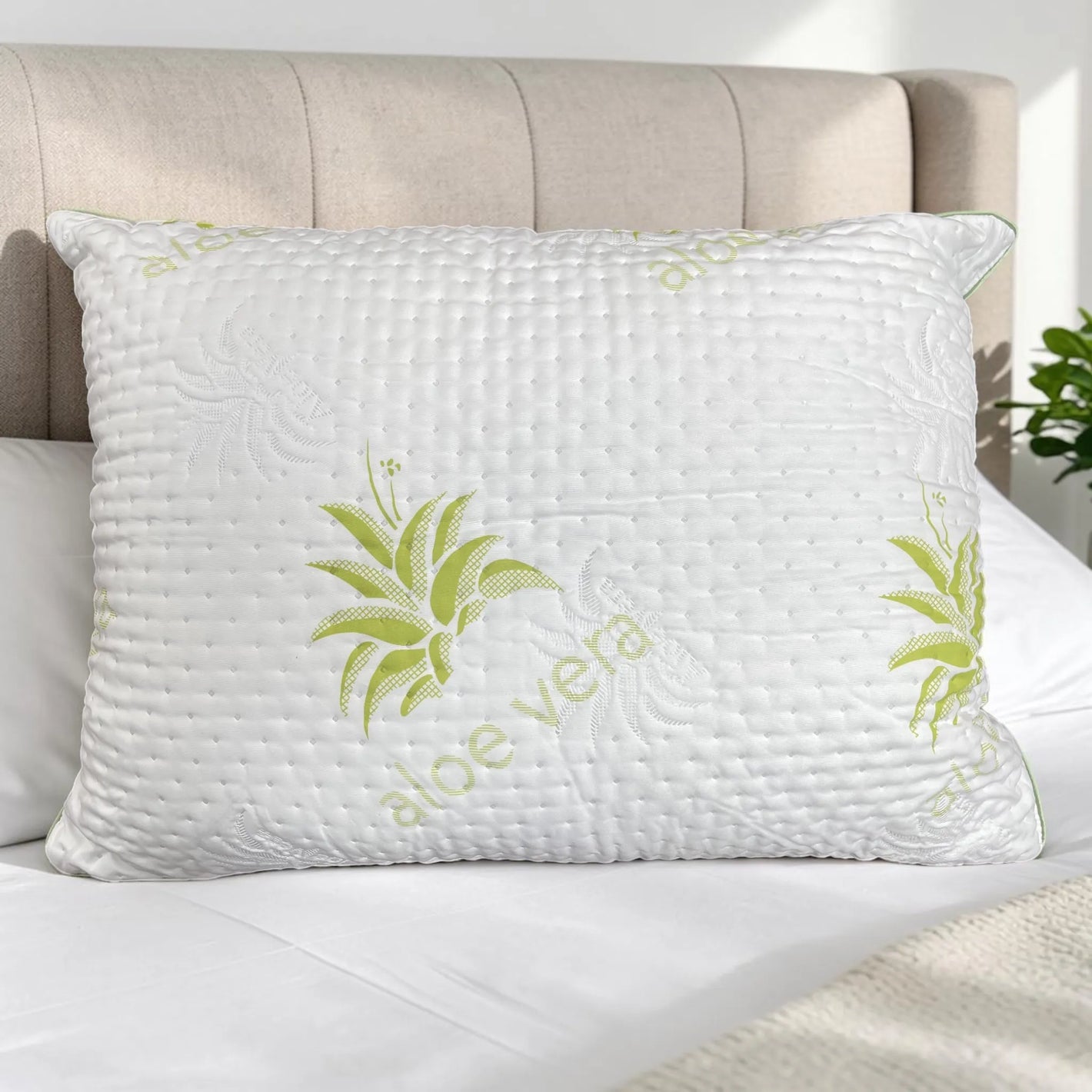 Almohada Aloe Vera Scarlett Classics Standard 51x66 cm color blanco con diseño verde, textura acolchada, hipoalergénica y respirable sobre cama blanca con cabecera beige.