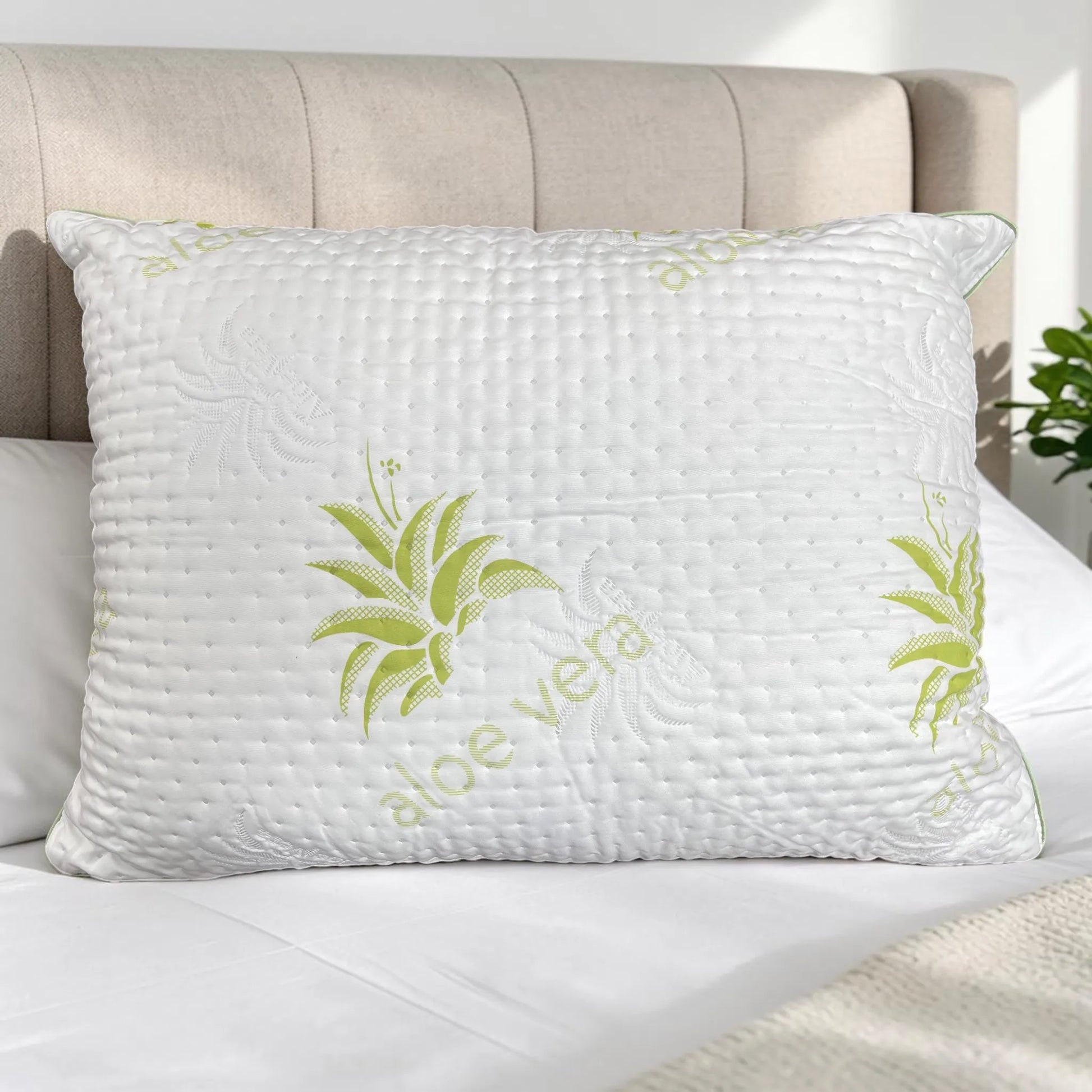 Almohada Aloe Vera Scarlett Classics Standard 51x66 cm color blanco con diseño verde, textura acolchada, hipoalergénica y respirable sobre cama blanca con cabecera beige.