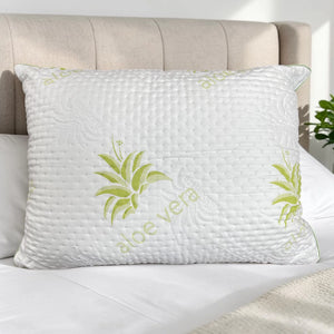 Almohada Aloe Vera Scarlett Classics Standard 51x66 cm color blanco con diseño verde, textura acolchada, hipoalergénica y respirable sobre cama blanca con cabecera beige.