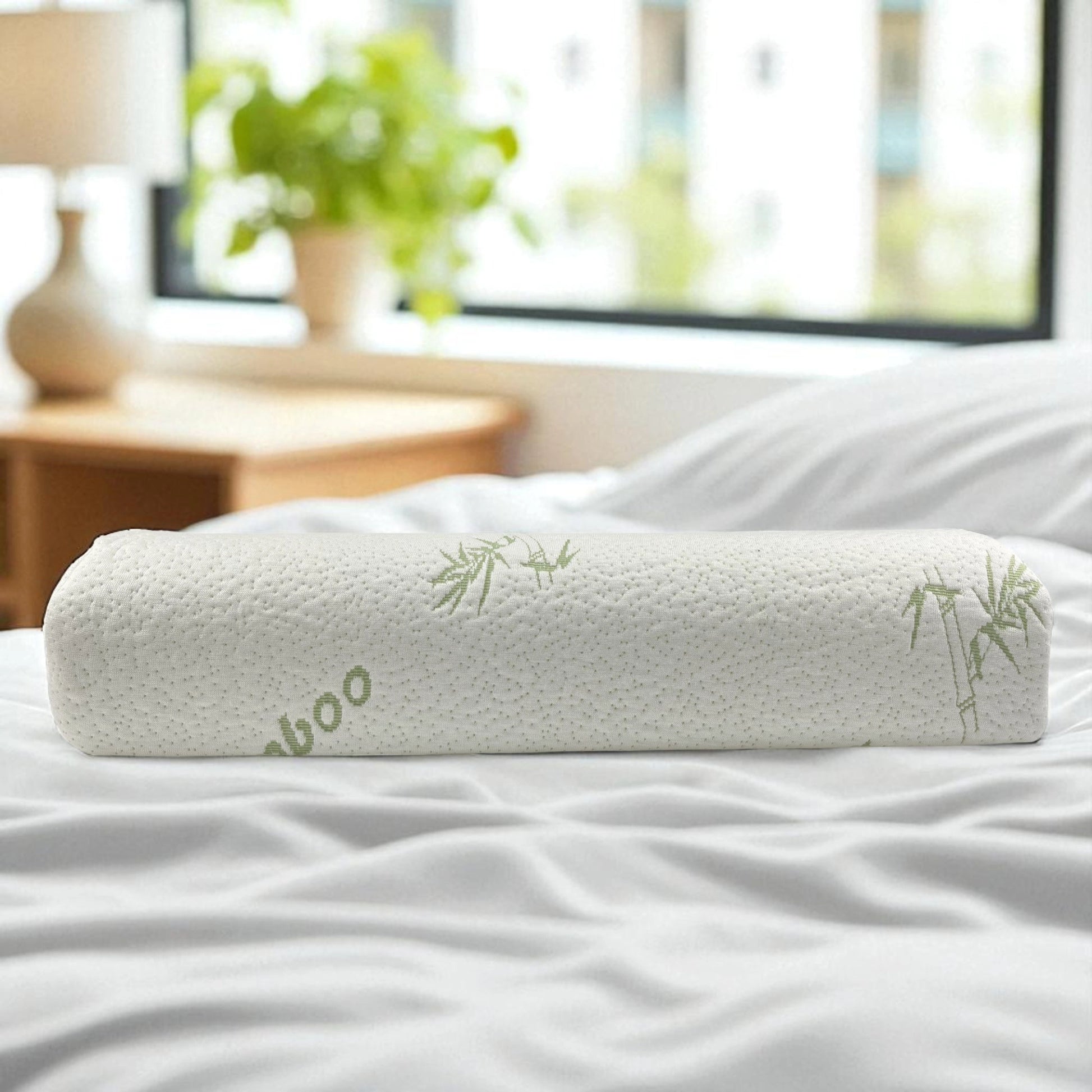 Vista cilíndrica enrollada de la almohada ortopédica memory foam con funda de bambú sobre cama blanca, marca Casa Opal, tamaño 47x30 cm