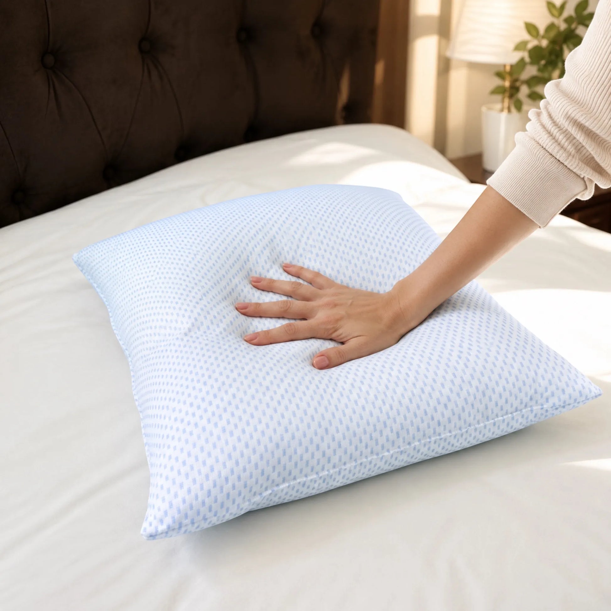 Mano presionando una almohada refrescante Pacific Home blanca con patrón celeste para demostrar su suavidad y soporte.