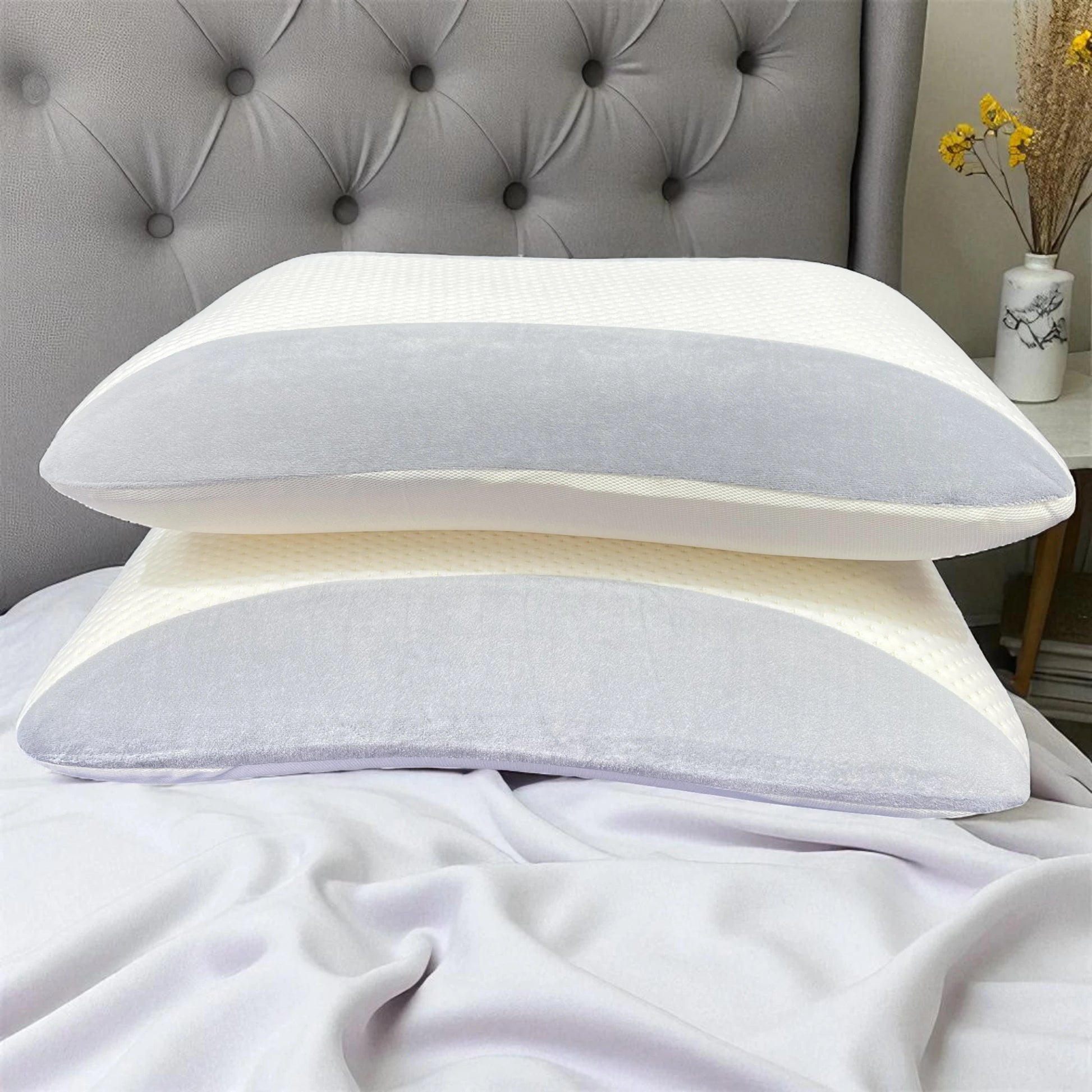 Par de almohadas Casa Opal memory foam 35x55 cm, blanco con gris, apiladas sobre cama en dormitorio con cabecera capitonada.