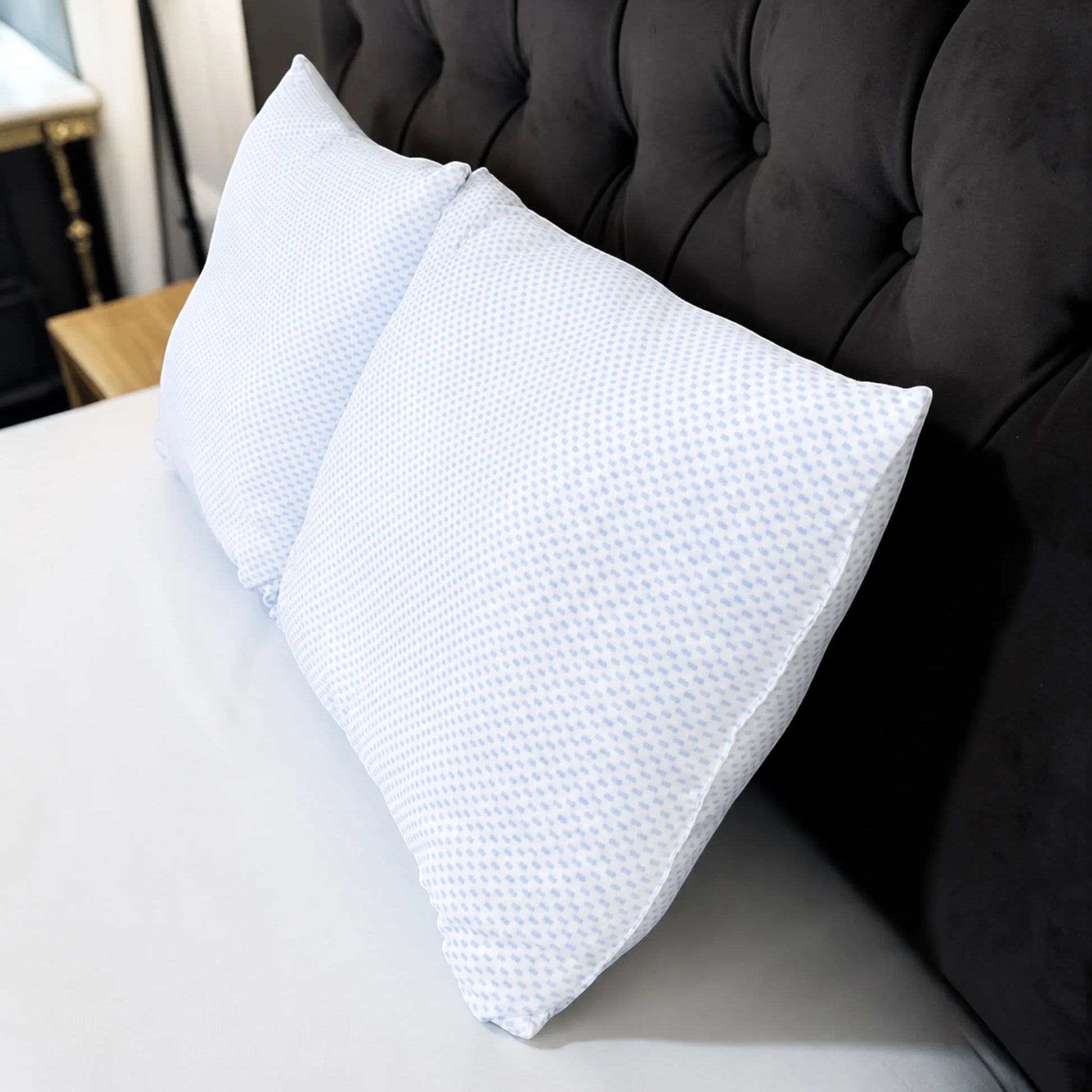 Dos almohadas refrescantes Pacific Home blancas con diseño celeste colocadas sobre una cama junto a una cabecera negra.