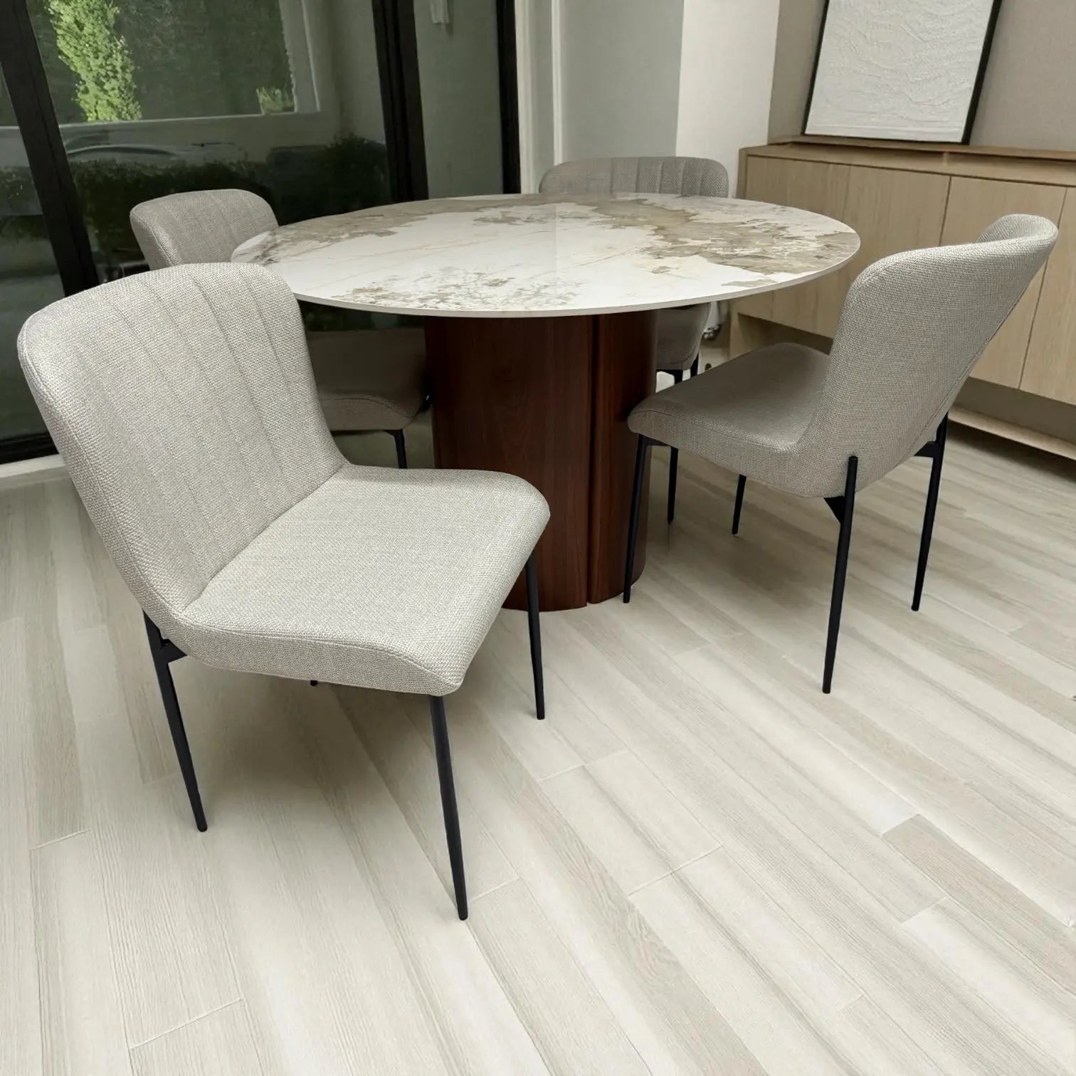 Vista superior del juego de comedor DT-04-2258 con mesa Ø120 cm efecto mármol y base nogal, sillas beige y aparador tono roble al fondo.