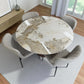Juego de comedor DT-04-2258 frente a ventanal: mesa redonda Ø120 cm efecto mármol con base nogal y cuatro sillas beige de patas metálicas negras, estilo moderno.