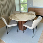 Juego de comedor Ambienta Home Decor DT-04-2258 con mesa redonda Ø120 cm efecto mármol, base en nogal y cuatro sillas beige de patas negras, vista lateral izquierda en ambiente.