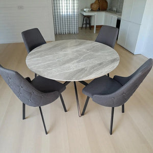 Set de comedor Ambienta Home Decor DT-04-2203 con mesa redonda de 120 cm, tablero acabado marmol blanco con vetas grises y 4 sillas tapizadas gris oscuro con patas metal negras; vista frontal izquierda en comedor.