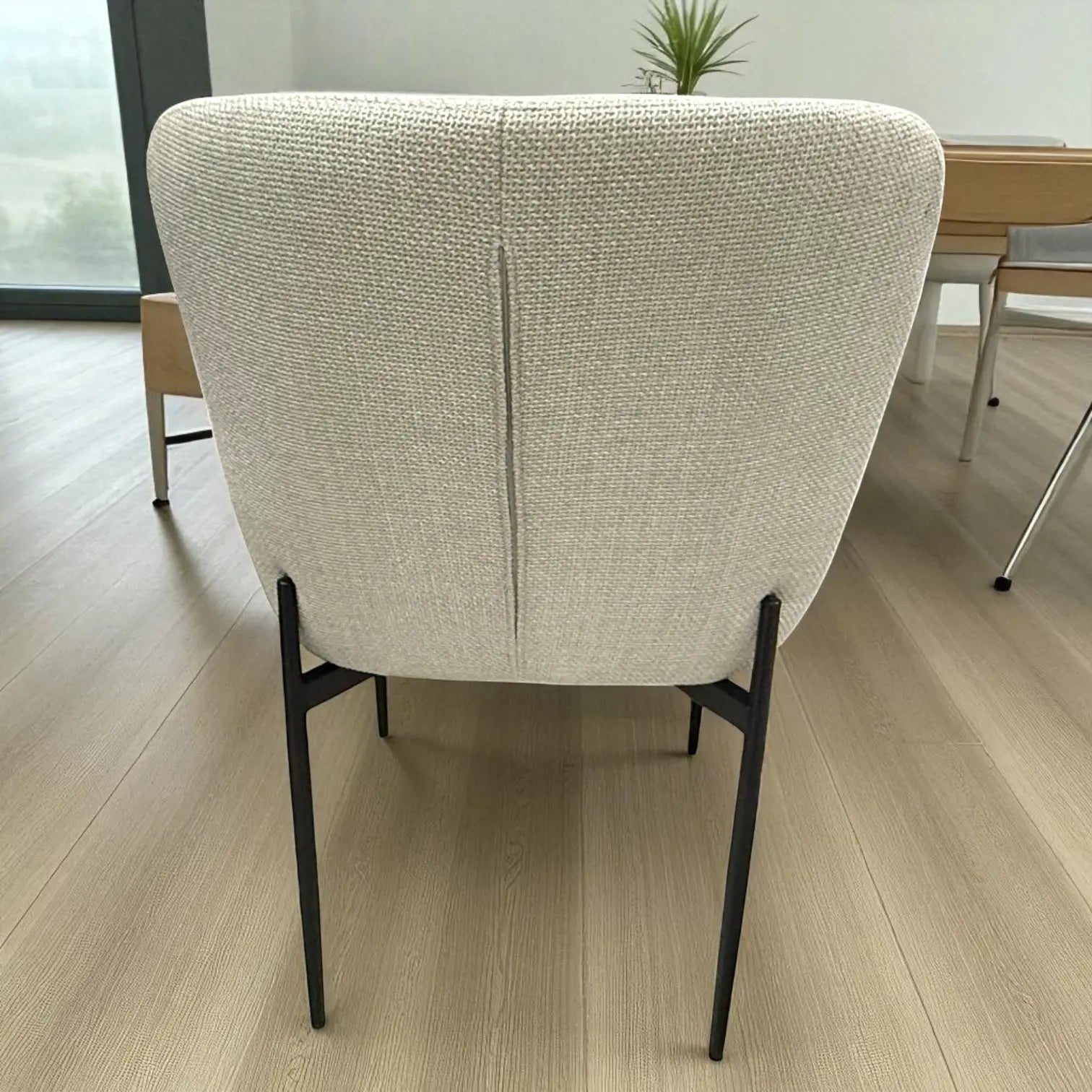 Vista trasera de la silla DT-04-2258 con respaldo curvo tapizado beige y costura central; estructura y patas metálicas negras, altura 82 cm, ancho 55 cm.