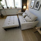 Sofá cama SFB-6096 beige en vista 3/4, modo cama con mecanismo y estructura metálica visible debajo.