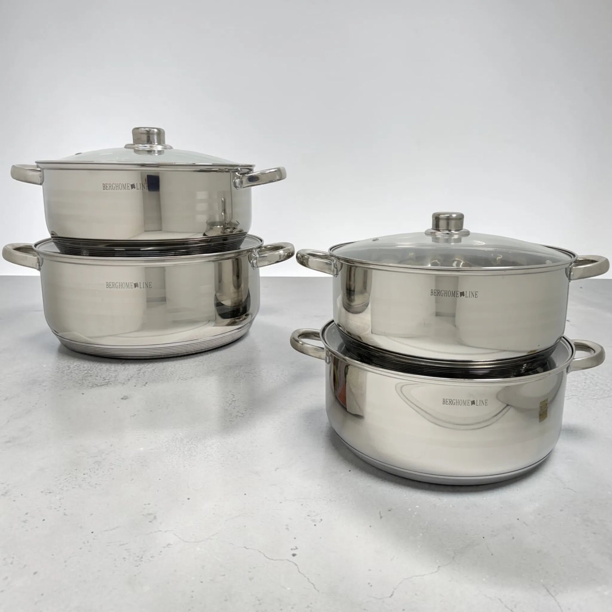 Batería de ollas BergHome Line BL-1465 de acero inoxidable apiladas en pares, con tapas de vidrio y acabado plateado brillante.