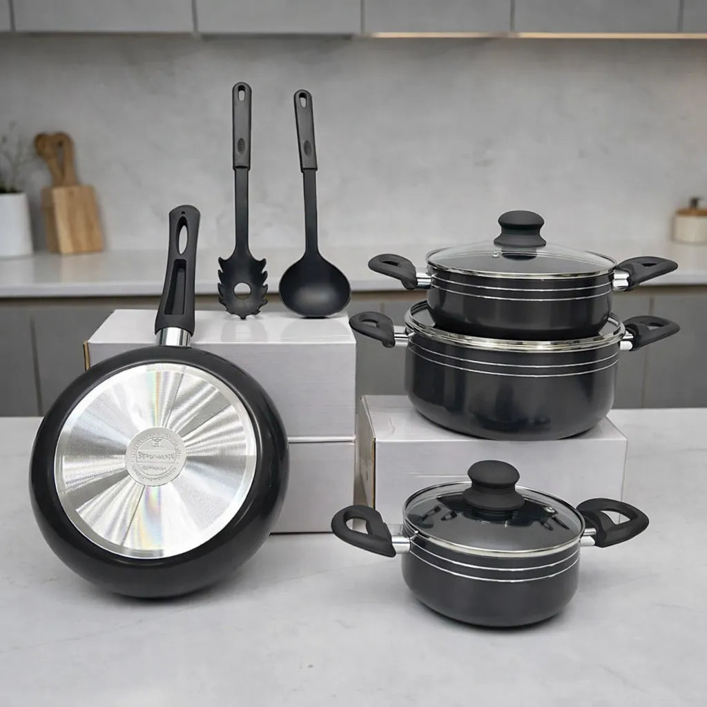 Batería de cocina Bergmann 9 piezas color negro con ollas y cacerolas con tapas de vidrio templado, sartén y dos utensilios, vista frontal en encimera.