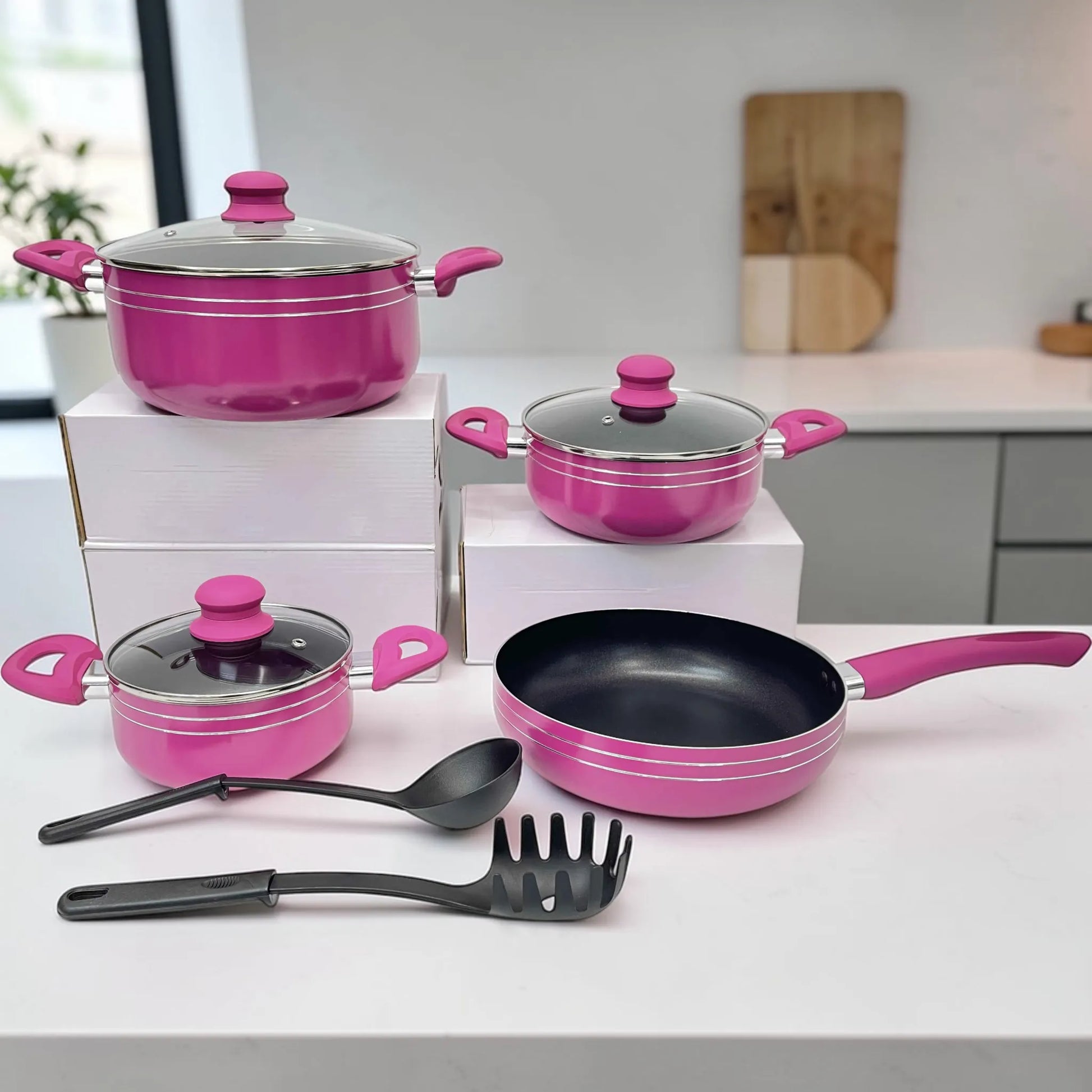 Batería de cocina Bergmann 9 piezas de aluminio antiadherente color fucsia, set completo con ollas y cacerolas con tapas de vidrio templado, sartén y utensilios, vista frontal en cocina.