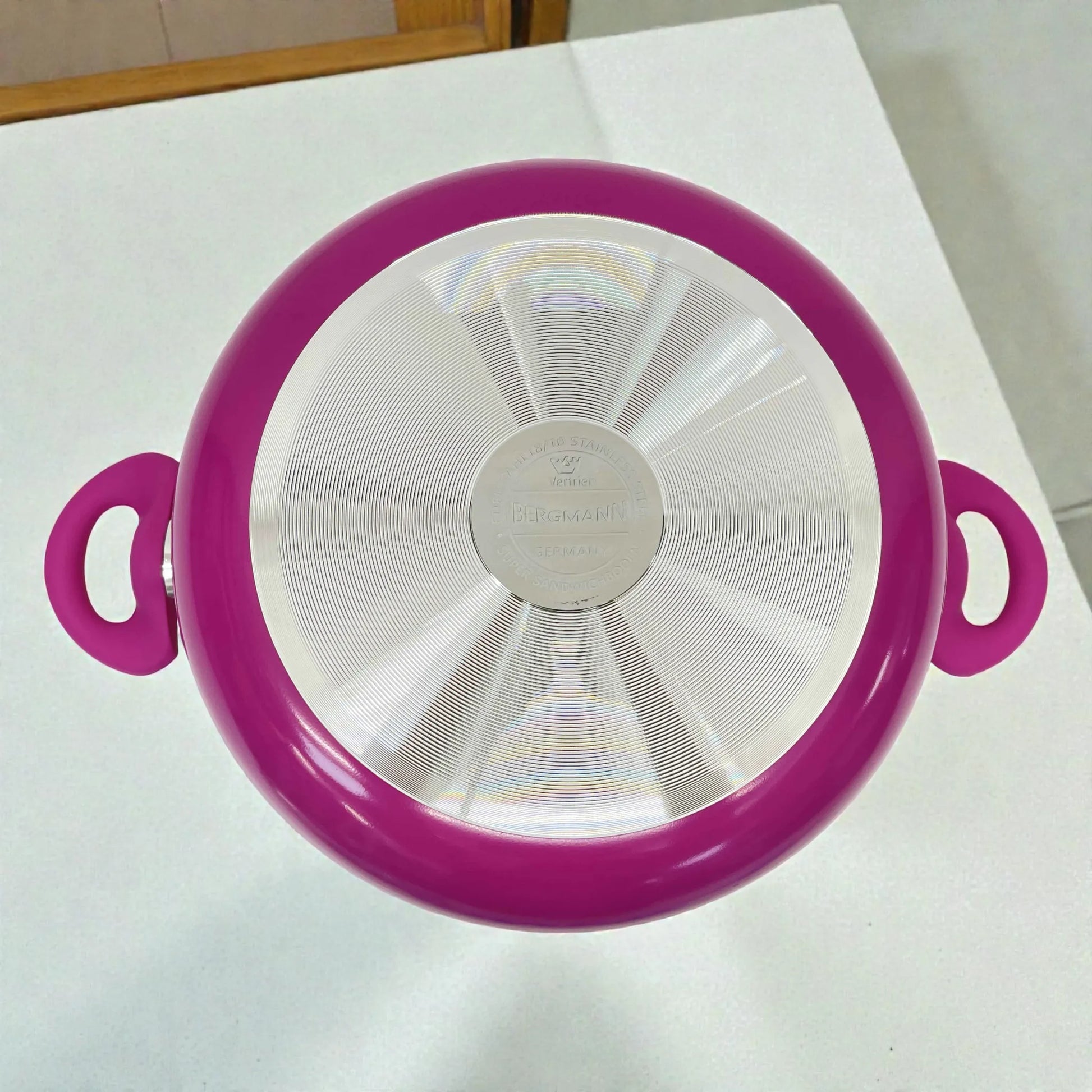 Base metálica de olla o cacerola Bergmann de aluminio antiadherente color fucsia con asas laterales resistentes al calor, vista inferior mostrando logo Bergmann y difusor de calor.