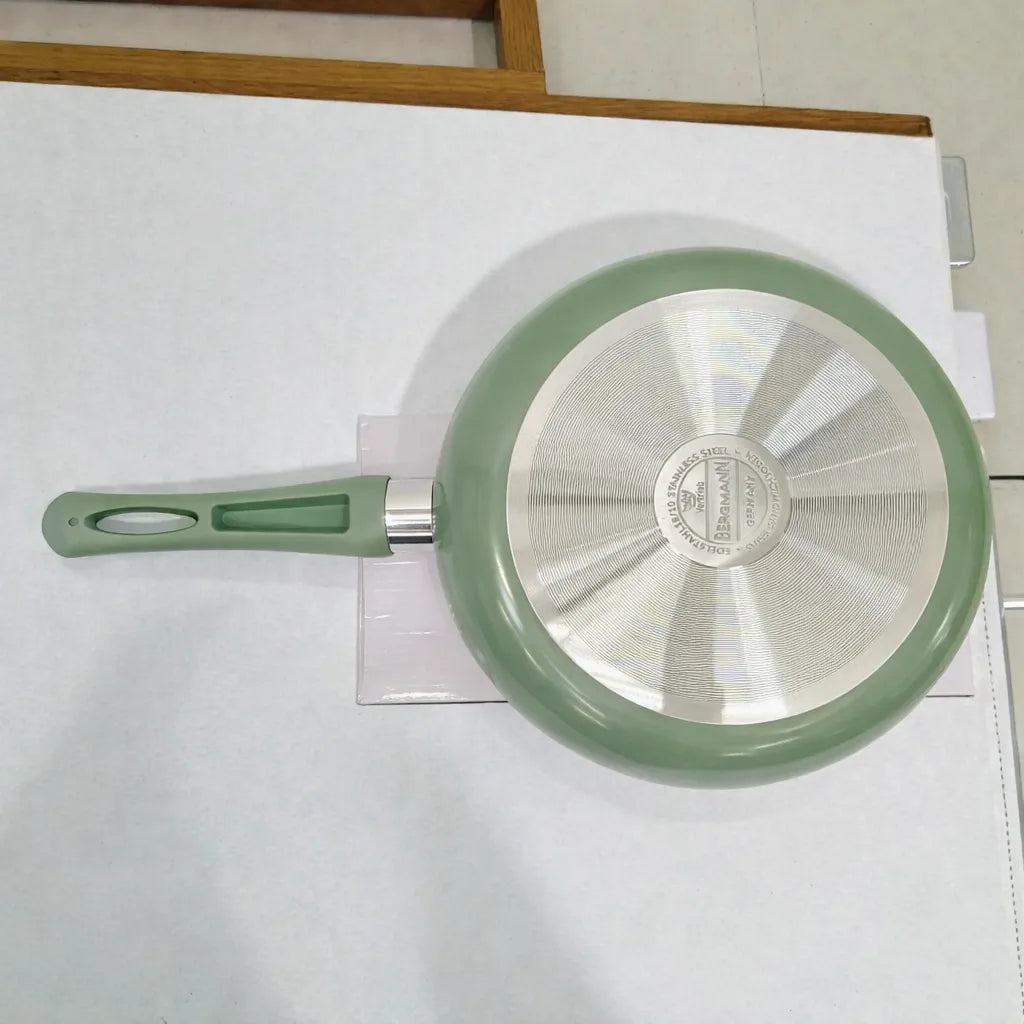 Base metálica del sartén Bergmann verde oliva con difusor de calor y logo Bergmann grabado al centro, vista inferior.