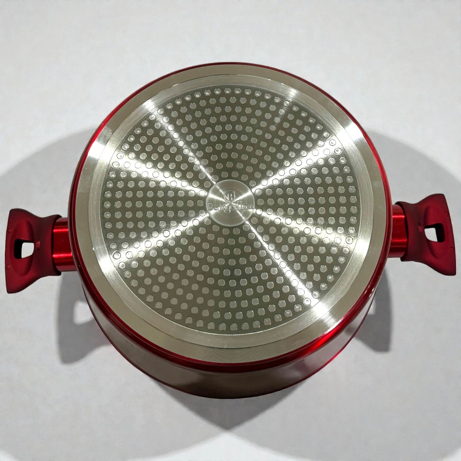 Vista inferior de olla Berlinger Haus rojo burgundy con dos asas laterales y base metálica para inducción en fondo blanco.