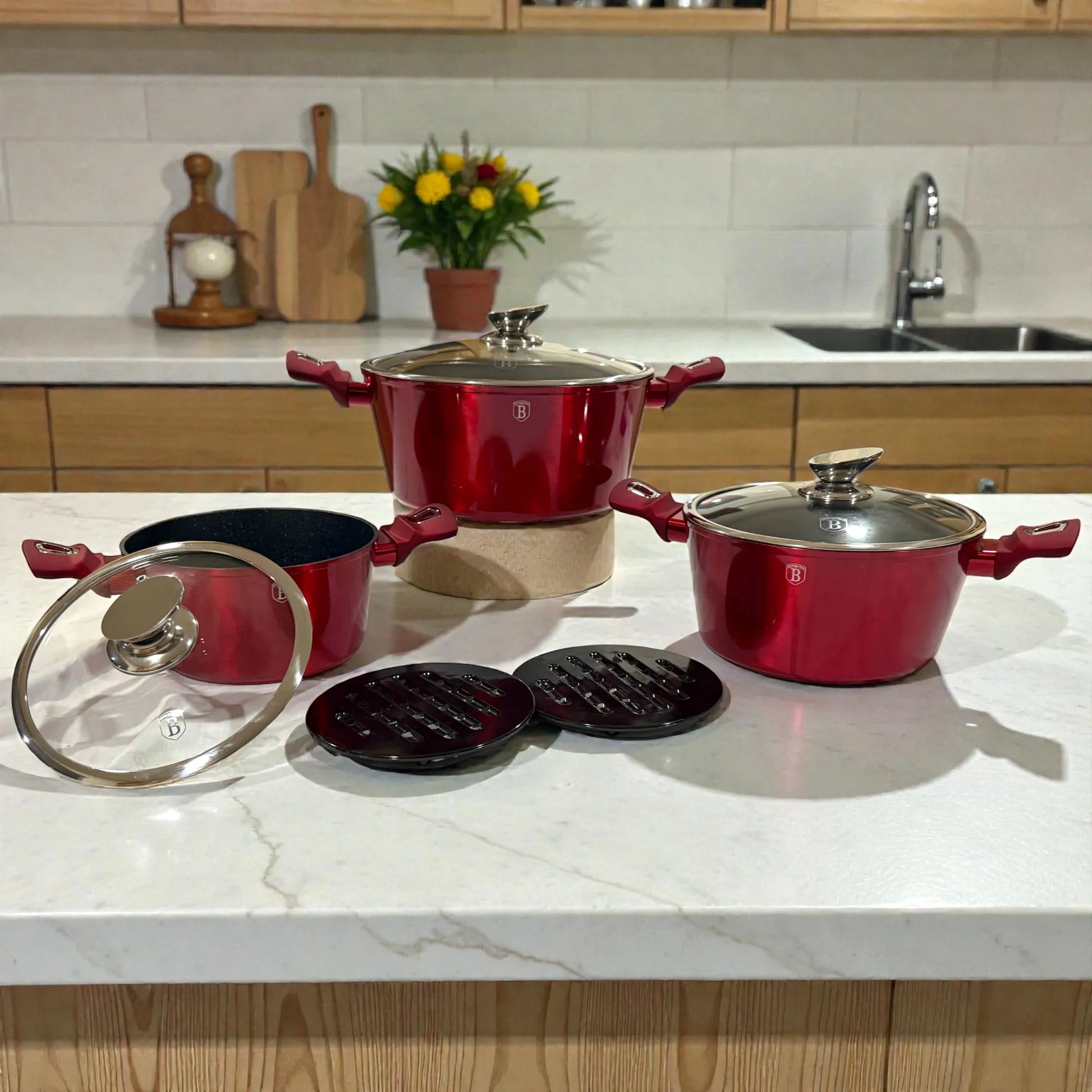 Cacerolas Berlinger Haus Metallic Line Burgundy con tapas de vidrio (20, 24 y 28 cm) y 2 bases de baquelita sobre encimera, color borgona metalizado con asas ergonomicas.