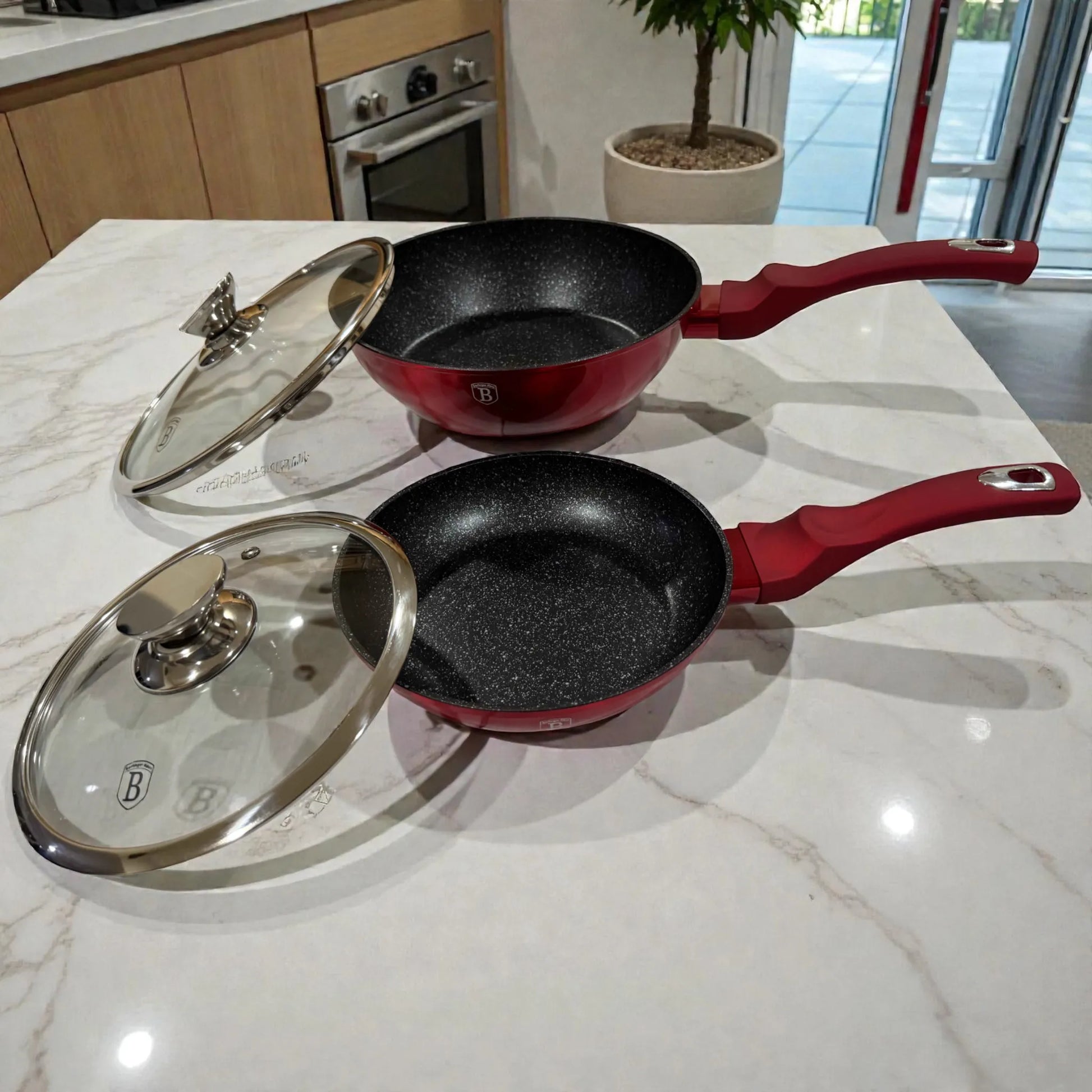 Sarten 20 cm y sarten honda 24 cm Berlinger Haus Metallic Line Burgundy con tapas de vidrio al lado, vista lateral sobre encimera, interior negro con recubrimiento antiadherente tipo marmol.
