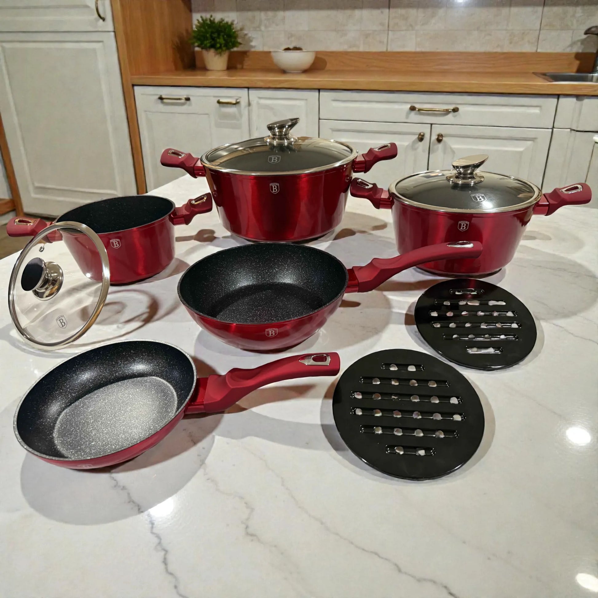 Set Berlinger Haus Metallic Line Burgundy en encimera, toma en angulo 3/4 mostrando cacerolas con tapa (20, 24 y 28 cm), sarten 20 cm, sarten honda 24 cm y bases de baquelita, acabado rojo borgona metalizado.