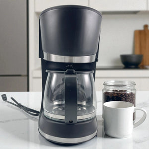 Cafetera eléctrica Sankey CM-1227 de 12 tazas color negro, vista frontal, acompañada de taza blanca y frasco de café en grano.