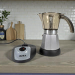 Cafetera moka eléctrica MOKA 3–6 tazas con base calefactora independiente; jarra superior transparente ahumada y cuerpo plateado sobre encimera de cocina.