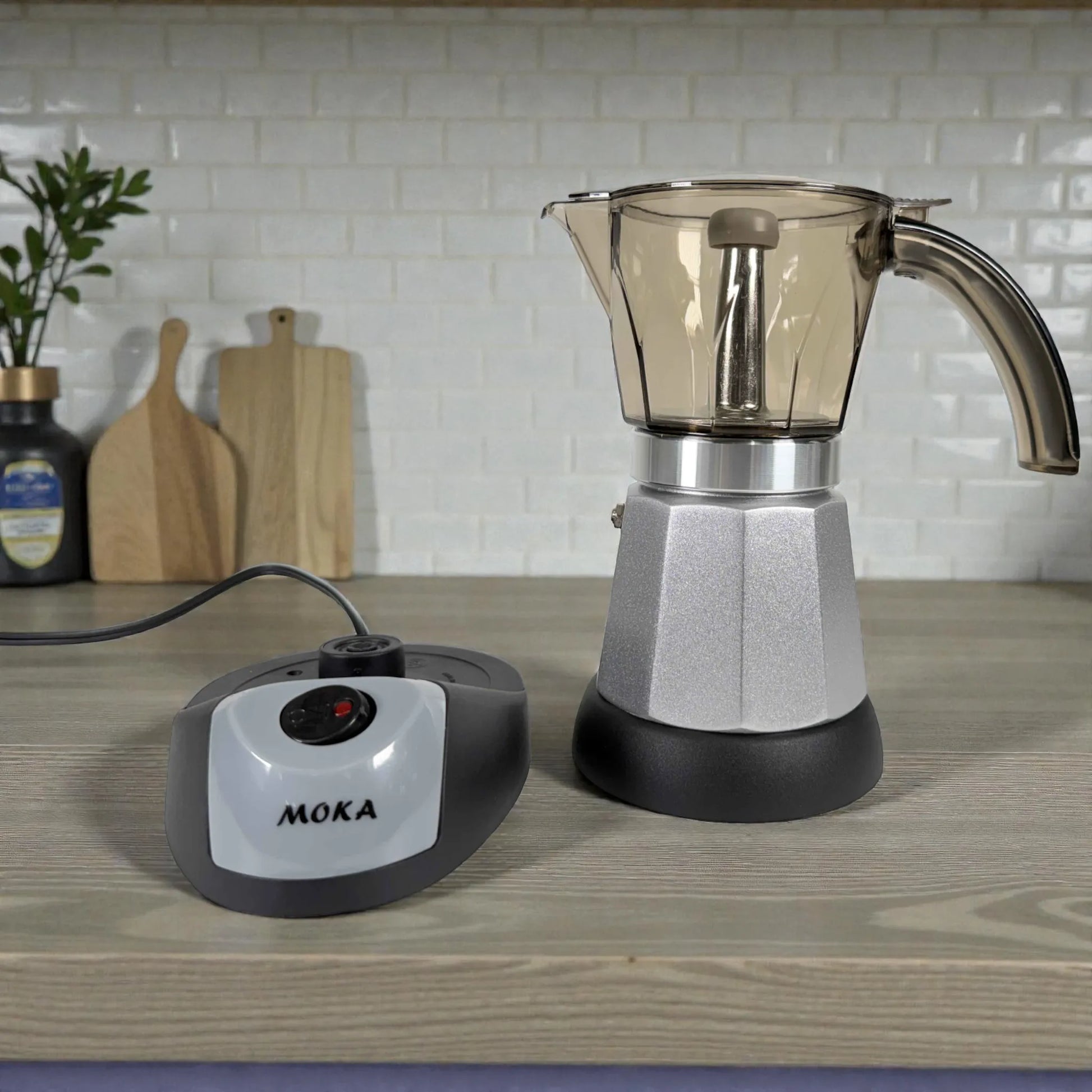 Cafetera moka eléctrica MOKA 3–6 tazas con base calefactora independiente; jarra superior transparente ahumada y cuerpo plateado sobre encimera de cocina.