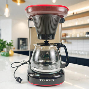 Cafetera Taurus Velvet Coffee 1.2L para 12 tazas, color negro con rojo, vista frontal con jarra de vidrio y cable eléctrico visible.