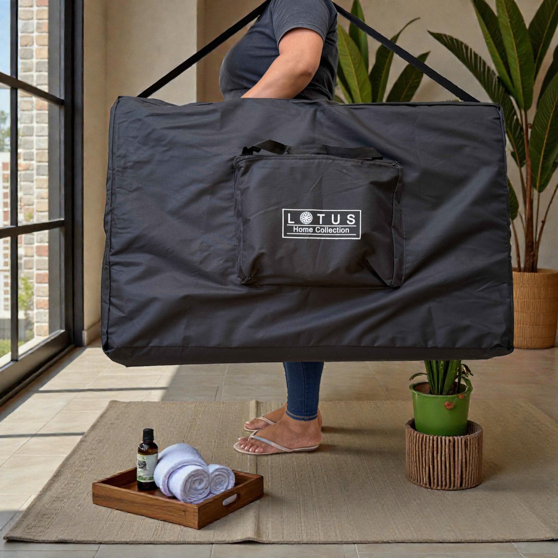 Persona cargando en el hombro la bolsa de transporte negra de la cama de masaje plegable Lotus Home Collection, demostrando su diseño portátil y fácil de mover.