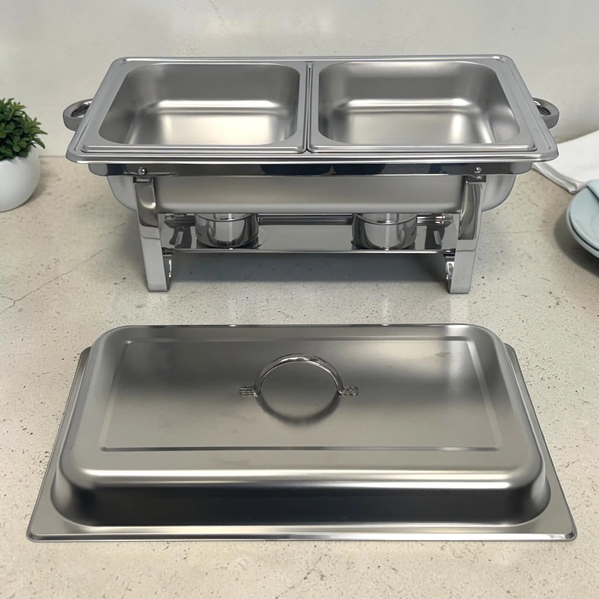 Chafing dish doble de acero inoxidable con tapa retirada al frente y dos bandejas listas para buffet.
