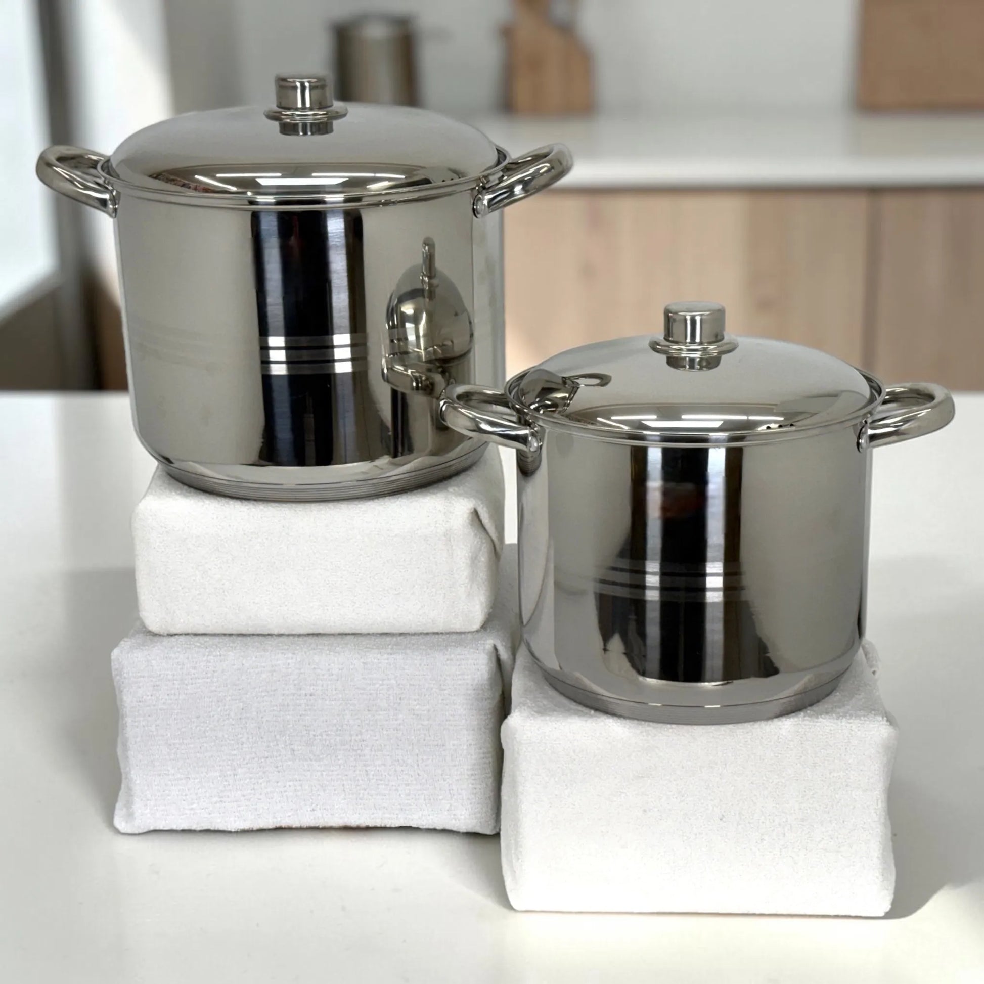 Dos ollas Crystal Cuisine CC-138 de acero inoxidable color plateado con tapa metalica, exhibidas individualmente sobre bases blancas en cocina iluminada.