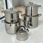 Set de ollas Crystal Cuisine CC-138 de acero inoxidable de 10 piezas en color plateado, con ollas grandes de 8L, 10L, 12L y 15L y tetera de 3L al frente, sobre encimera de cocina.