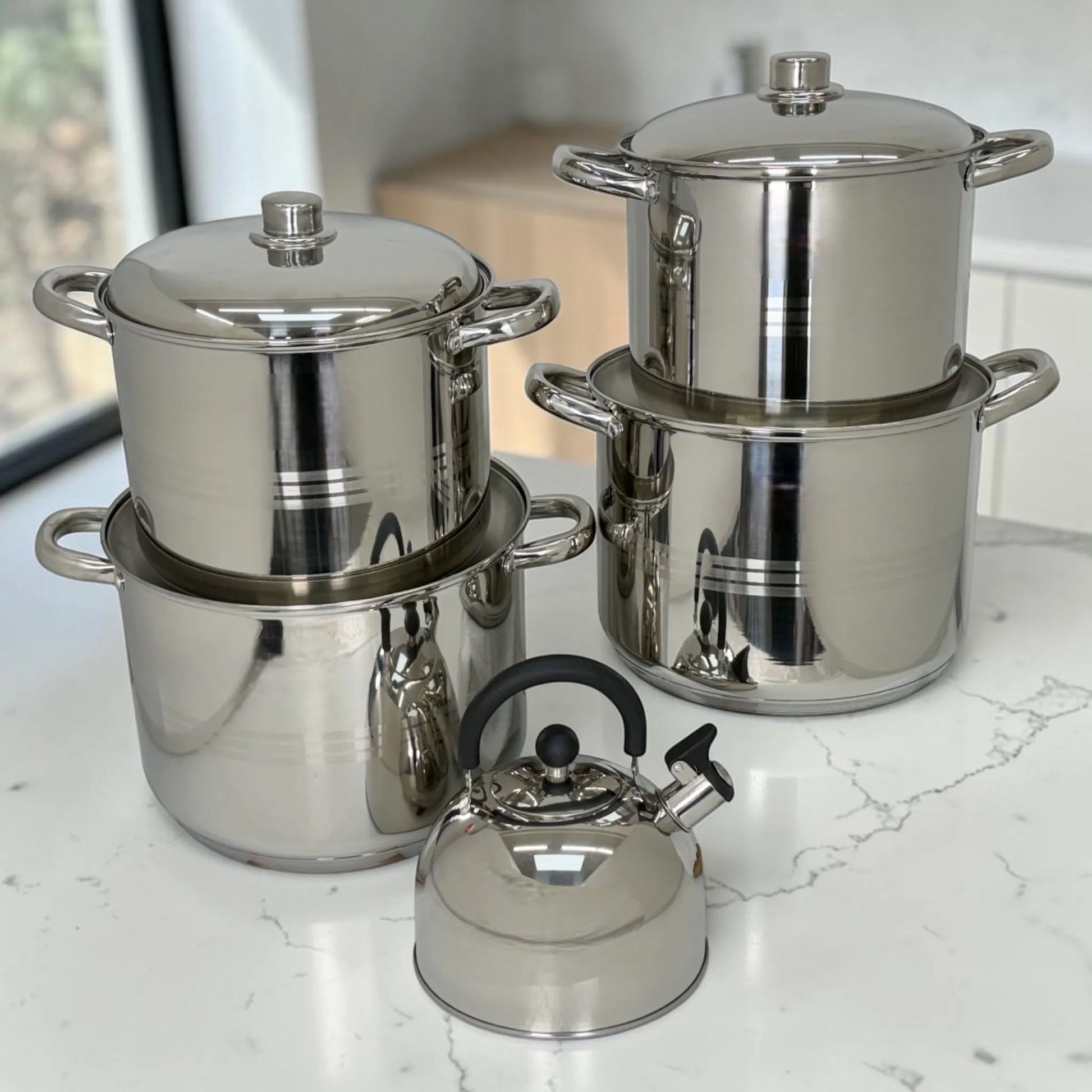 Set de ollas Crystal Cuisine CC-138 de acero inoxidable de 10 piezas en color plateado, con ollas grandes de 8L, 10L, 12L y 15L y tetera de 3L al frente, sobre encimera de cocina.