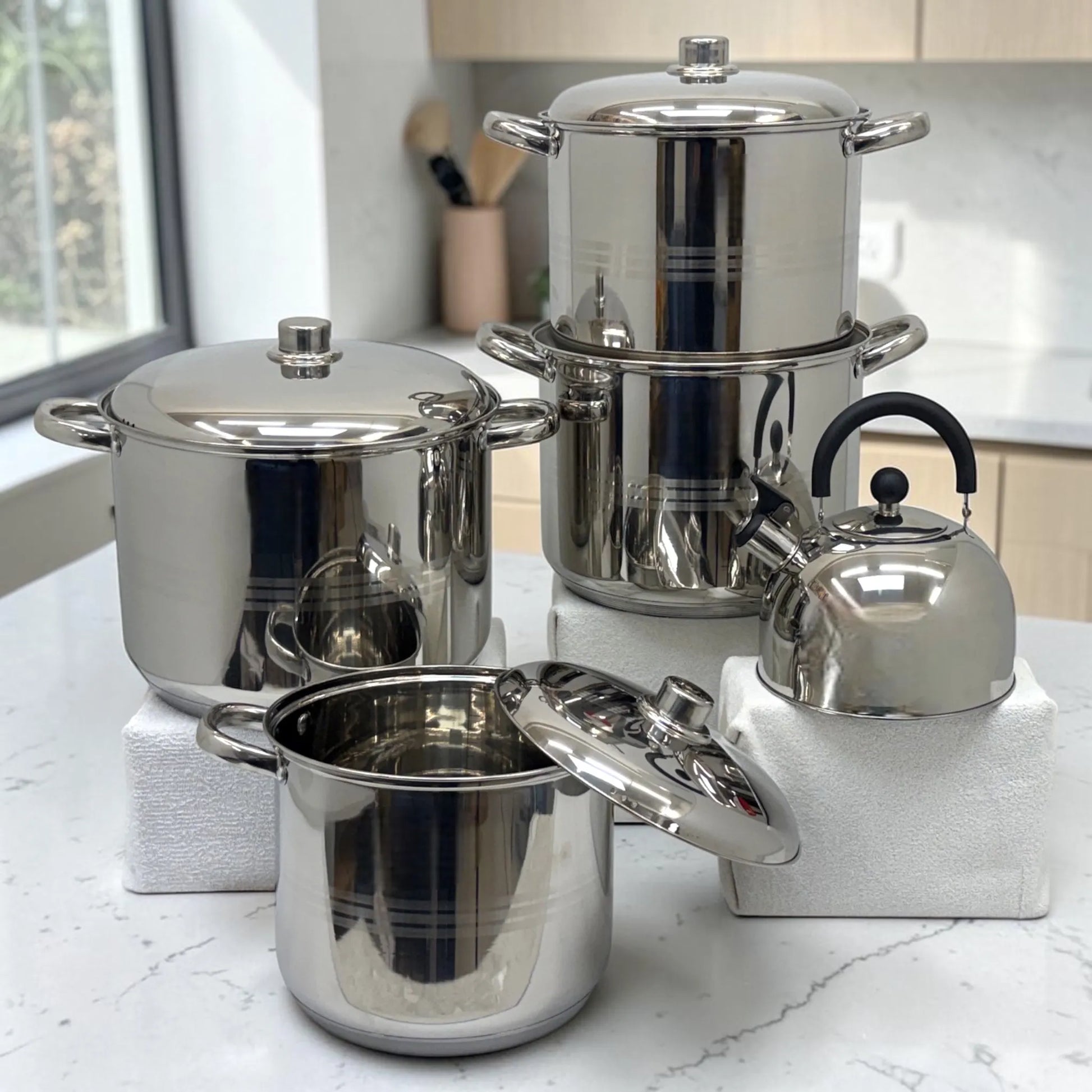 Juego de ollas Crystal Cuisine CC-138 de acero inoxidable de 10 piezas con tetera, vista frontal completa con cuatro ollas de distintos tamanos y tapas metalicas sobre mesa de cocina.