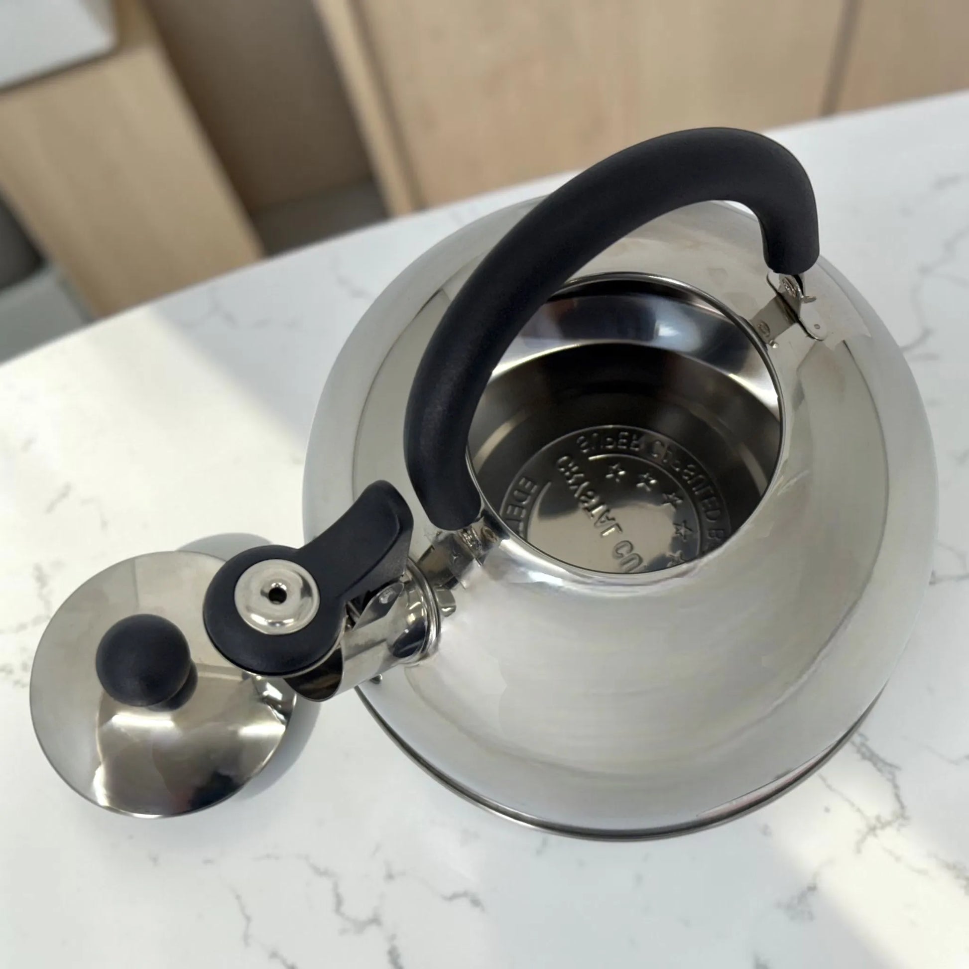 Vista superior de tetera Crystal Cuisine CC-138 de acero inoxidable de 3 litros con tapa abierta, asa negra y boquilla con silbato.