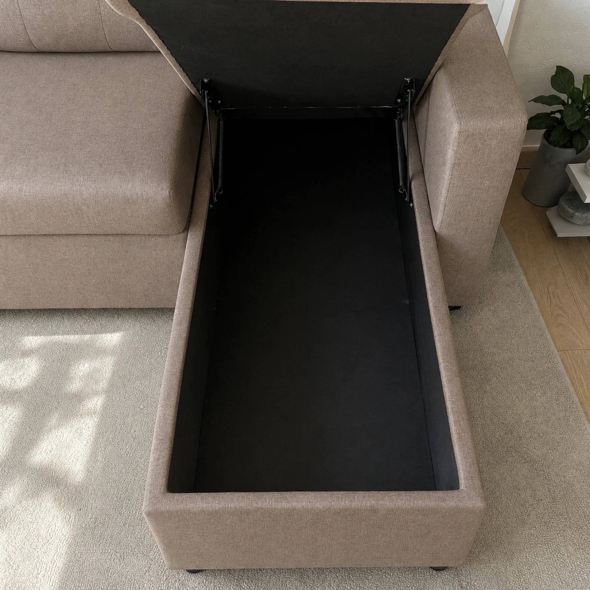 Sofá cama Ambienta Home Decor color taupe con cajón lateral abierto, vista diagonal, interior negro, mecanismo de apertura y diseño moderno para sala.