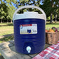 Dispensador térmico Princeware azul de 17 litros SKU 3554 con asa superior y grifo dispensador, colocado en mesa de picnic al aire libre.