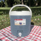 Vista frontal completa del dispensador térmico Princeware gris de 17 litros SKU 3554 con asa blanca, tapa superior y grifo dispensador.