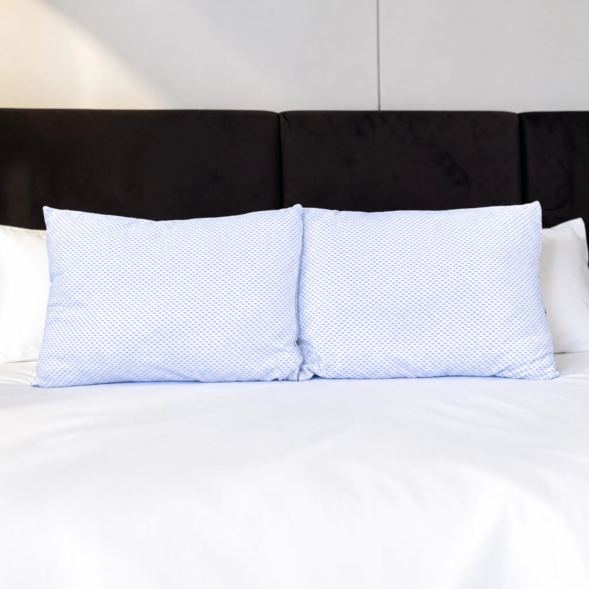 Dos almohadas refrescantes Pacific Home blancas con patrón celeste colocadas juntas sobre una cama con ropa blanca.